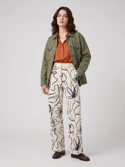 A Western model with dark‑brown hair, solid‑color background #efefef, stylish outfit, medium shot. No plain white T‑shirt or jeans. The model’s trousers feature a large hand‑drawn‑style pattern.