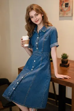Create a product model image of a denim dress. The model should be a young, beautiful, playful, and sweet Caucasian woman. The background can be any everyday setting. The model should be holding a coffee cup in one hand and resting the other hand on a walnut-colored table, with one leg casually crossed over the other. She should be leaning casually against the table or wall. The overall lighting should be somewhat dim, creating a retro yet sweet atmosphere with a film poster-like quality.
